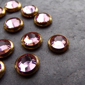 Può includere: Strass di vetro rosa con montature dorate. Gli strass sono disposti a semicerchio su una superficie grigia.