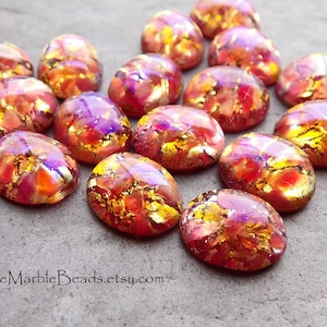 May include: A collection of 15 oval-shaped glass cabochons with a red, orange, and gold iridescent finish. The cabochons have a textured surface with gold flecks throughout.