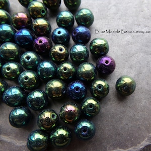 May include: A collection of iridescent glass beads in shades of green, blue, and purple. The beads are round and have a smooth, shiny finish.