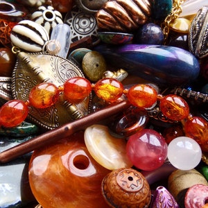 May include: A close-up of a variety of colourful beads and jewellery findings, including amber, glass, metal, and wood. The beads are arranged in a random pattern, creating a visually appealing and textured composition.
