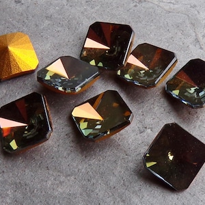 May include: An assortment of faceted, square-cut crystals in shades of brown, gold, and iridescent hues. One crystal has a textured, golden surface. The crystals are arranged on a gray surface, showcasing their reflective qualities.