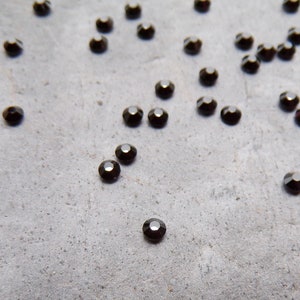 Peut inclure: Une dispersion de petits strass ronds noirs sur une surface grise.