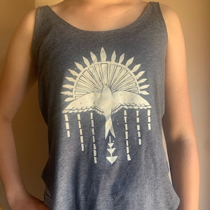May include: A gray tank top with a white graphic of a bird flying above a sunburst design. The graphic also includes a series of vertical lines and a triangle shape.