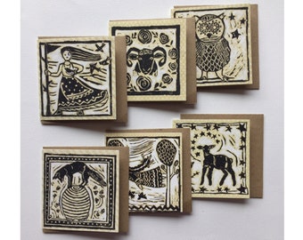 May include: Set of six black and white illustrated greeting cards with a rustic brown paper backing. The cards feature various illustrations including a woman with a staff, a ram, an owl, a deer, a fox, and a lamb.