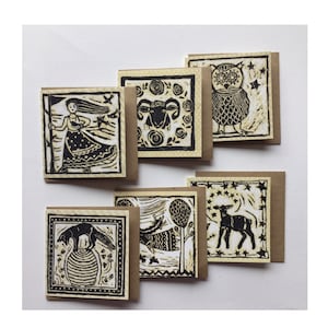 May include: Set of six black and white illustrated greeting cards with a brown paper backing. The cards feature a variety of images including a woman with a staff, a ram, an owl, a deer, a fox, and a tree.