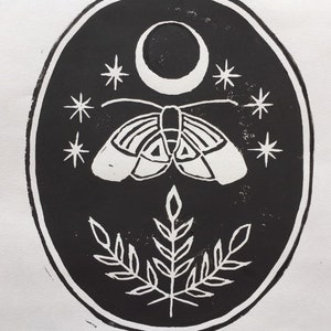 May include: Black and white print of a moth with a crescent moon and stars above it. The moth is centered in the oval-shaped print with a stylized plant below it. The print is signed "Celestine".