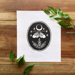 May include: Black and white print of a moth with a crescent moon and stars in a circle. The print is titled "Celestial" and signed by the artist.