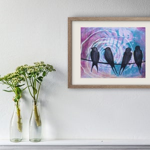 May include: A framed artwork featuring four black birds perched on a wire against a colorful abstract background of pink, blue, and white. The artwork is in a light brown wooden frame and is displayed on a white wall.