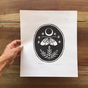 May include: Black and white print of a moth with wings spread, a crescent moon, and stars in a circle. The print is signed "Celestini" in the bottom right corner.