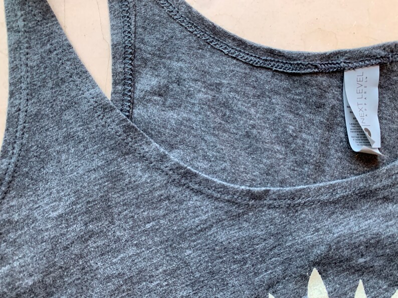 May include: A gray tank top with a white graphic print and a tag that reads "NEXT LEVEL" on the shoulder.