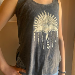 May include: A gray tank top with a white graphic of a bird flying through a sunburst design. The graphic also includes a series of vertical lines and arrows.