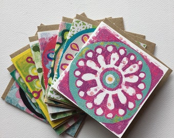 May include: A stack of colorful greeting cards with a variety of floral designs. The cards are printed on white paper and have a brown paper backing.