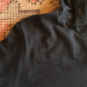 May include: Close-up of a black hooded sweatshirt with a seam down the back.
