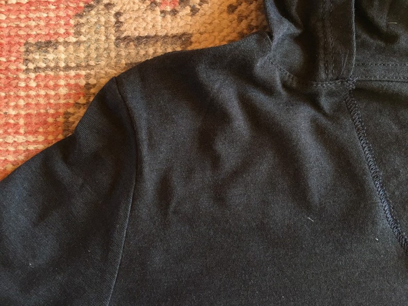 May include: Close-up of a black hooded sweatshirt with a seam down the back.