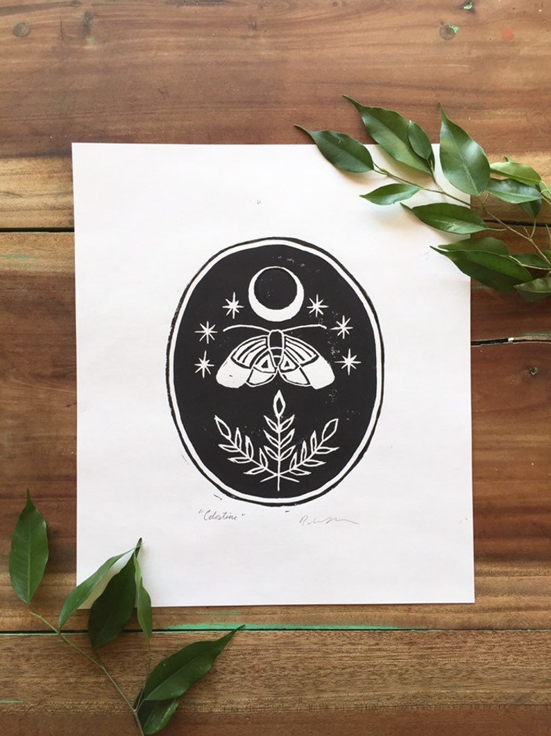 May include: Black and white print of a moth with a crescent moon and stars in a circle. The print has the word "Celestine" written below the image.