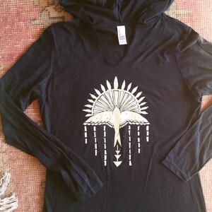 May include: Black long-sleeved hooded shirt with a white graphic of a bird with a sunburst design and arrows.