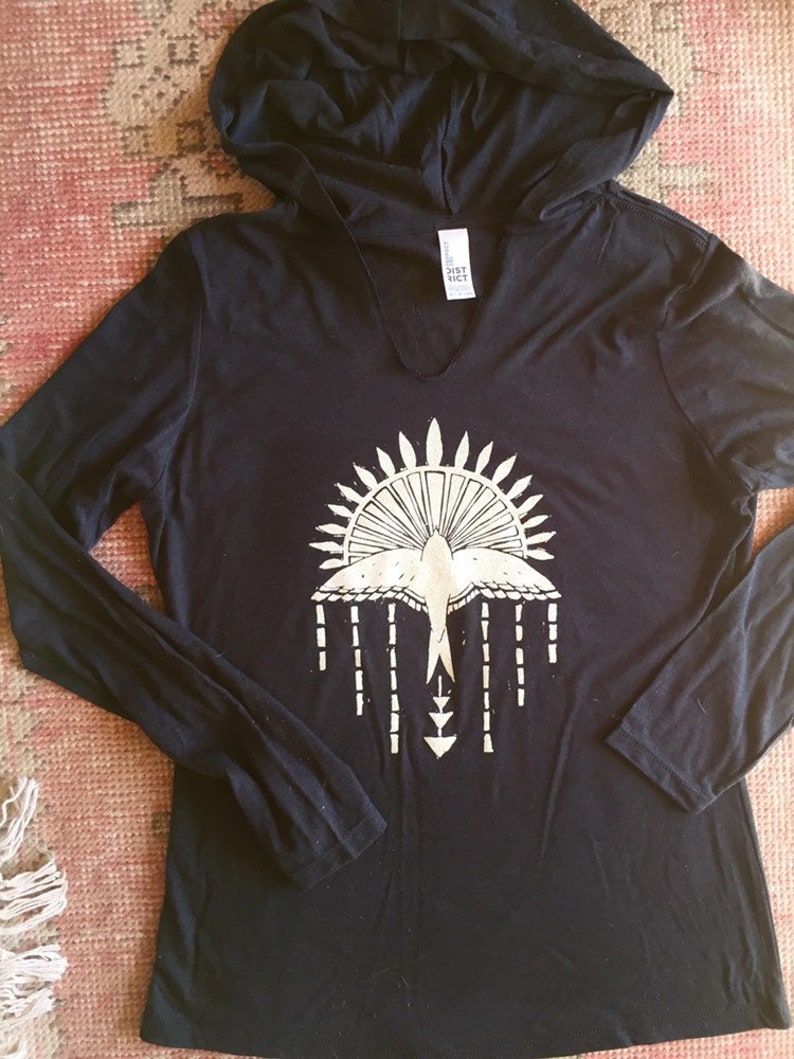 May include: Black long-sleeved hooded shirt with a white graphic of a bird with a sunburst design and arrows.