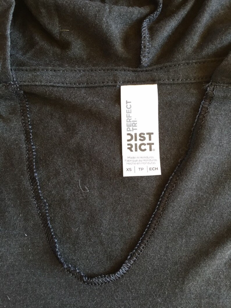 May include: A black hooded sweatshirt with a white tag that reads "PERFECT TRI. DISTRICT" and size information: XS, TP, ECH. The tag is attached to the neckline of the sweatshirt.