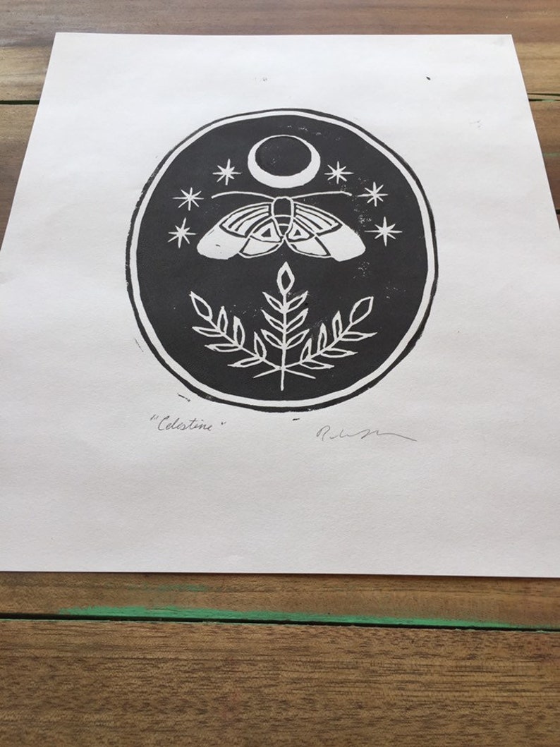 May include: Black and white print of a moth with wings spread, a crescent moon, and stars on a dark background. The print is in a circle with a plant at the bottom. The text "Celestine" is written below the circle.
