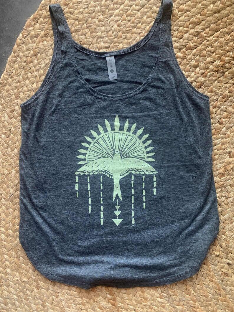 May include: A dark gray tank top with a light green graphic of a stylized bird with a sunburst design above it.