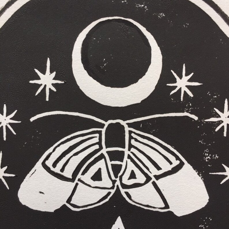 May include: Black and white linocut print of a moth with wings spread, flying under a crescent moon with stars in the background.