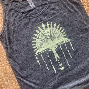 May include: A gray tank top with a green graphic of a bird flying out of a sun with a geometric design underneath.