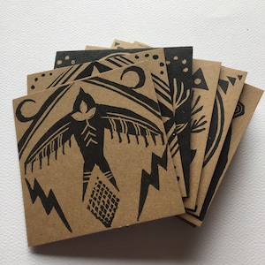 May include: A set of six brown paper cards with black ink illustrations. The cards feature a variety of designs, including a bird, lightning bolts, and geometric patterns.