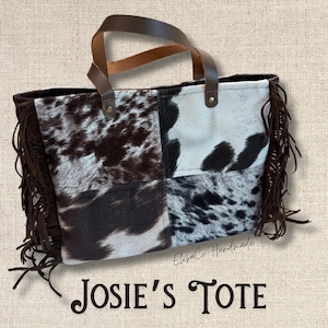 May include: A patchwork tote bag with a cowhide pattern in shades of brown, black, and white. The bag features brown leather handles and fringe detailing along the sides. The text "Josie's Tote" is displayed at the bottom.