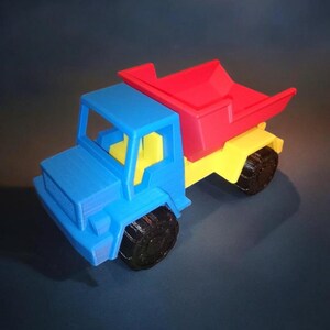 May include: A blue toy dump truck with a yellow bed and a red removable dump bed. The truck has black wheels.