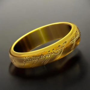 May include: A gold ring with an inscription in an ancient language. The inscription is in a cursive script and is visible on the outside of the ring.