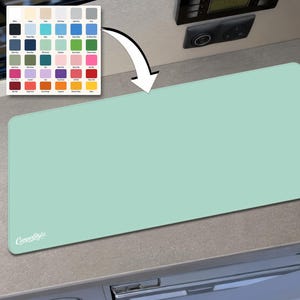 May include: A rectangular mint green desk mat with rounded corners and a stitched edge. The bottom left corner features the white text CamperStylz. A colour palette chart with forty-two distinct colour swatches is positioned above the mat.