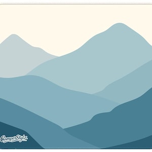 May include: A square mousepad with a layered mountain range design in shades of blue and a cream-coloured sky. The words "CamperStylz" are printed in white in the lower left corner. The mousepad has a stitched border.