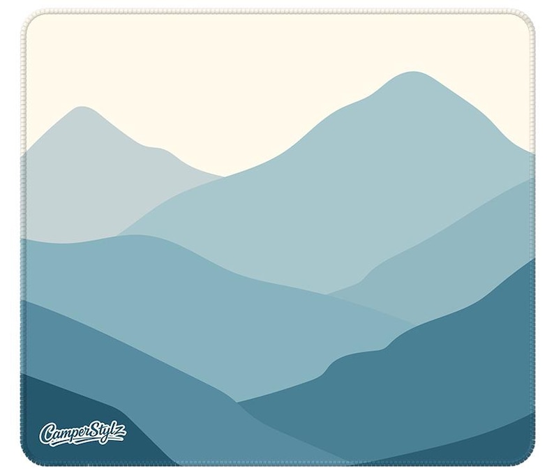 May include: A square mousepad with a layered mountain range design in shades of blue and a cream-coloured sky. The words "CamperStylz" are printed in white in the lower left corner. The mousepad has a stitched border.