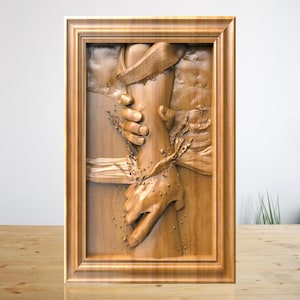 May include: A wooden relief carving depicting two hands reaching out to each other, framed in a light brown wooden frame. The carving has a 3D effect, with details of water and fabric. The artwork is displayed on a wooden surface.