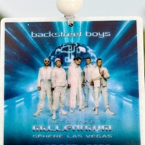 May include: A square hanging ornament featuring a blue-toned graphic of the Backstreet Boys in white outfits. The text reads: backstreet boys, INTO THE MILLENNIUM, SPHERE LAS VEGAS, JUNE 25TH, 2026. A white bead is attached to the top with a silver string.