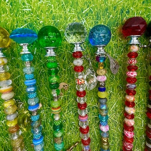 May include: A collection of decorative bottle stoppers with colorful glass and beaded designs. Each stopper features a unique, faceted glass top in shades of yellow, blue, green, and red. The stems are adorned with various beads and charms.