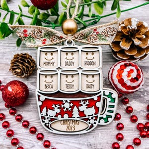 May include: Wooden Christmas ornament shaped like a mug, with the text "Christmas 2023." The ornament features six smiling faces with names: Mommy, Daddy, Hudson, Becca, Teddy, and Daisy. The mug design includes reindeer and snowflakes.