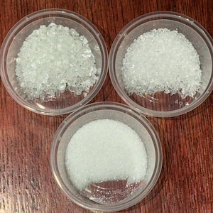 May include: Three clear plastic bowls filled with white crystals. The crystals in the bowls are different sizes and shapes.