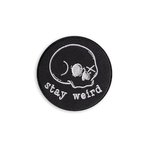 May include: Black and white embroidered patch with a skull and the text "stay weird".