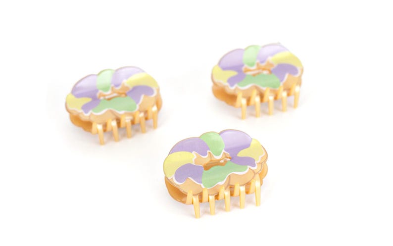 Op de afbeelding: Drie bloemvormige haarclips. Elke clip heeft een goudkleurige basis met tanden en een bloemenpatroon in paars, geel en groen. De clips zijn gerangschikt op een witte achtergrond.