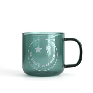 May include: A teal green glass mug with a black handle. The mug has a white smiley face with stars and a lightning bolt inside. The text "BE KIND & STAY WEIRD" is written around the smiley face.