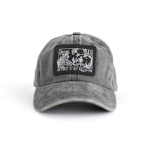 Peut inclure: Une casquette de baseball en denim noir délavé avec un patch brodé noir et blanc qui dit "Nature is my religion". Le patch représente un crâne entouré de fleurs et de feuilles.