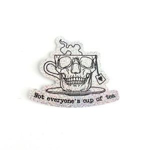 May include: A black and white sticker with a skull in a teacup. The text reads "Not everyone's cup of tea."