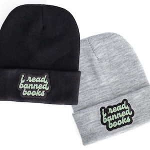 May include: Two knit beanies, one black and one gray, with a green "I read banned books" patch on the front.