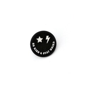May include: Black and white smiley face button with the text "Be Kind & Stay Weird" and a star and lightning bolt.