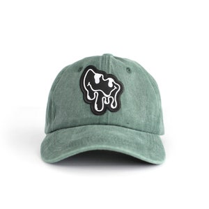 May include: A green baseball cap with a black and white dripping smiley face patch.