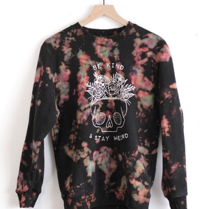 May include: Black tie-dye sweatshirt with a white skull graphic and the text "Be Kind & Stay Weird".
