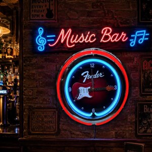 May include: A neon sign saying "Music Bar" in red and blue, above a clock with a Fender guitar design. The clock has a red and blue neon border. The background is a brick wall.