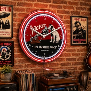 May include: A round wall clock with a red and black face featuring the Victor logo, a gramophone, and a dog with the text His Master's Voice. The clock has a bright red neon border, white hour and minute hands, and black numerals from 1 to 12.