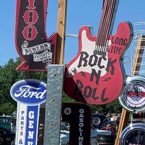 May include: A display of vintage signs, including a red and white guitar-shaped sign with "Rock N Roll" text, a "Tattoo Parlor" sign, and a Ford sign. Other signs include "Texaco" and clocks.